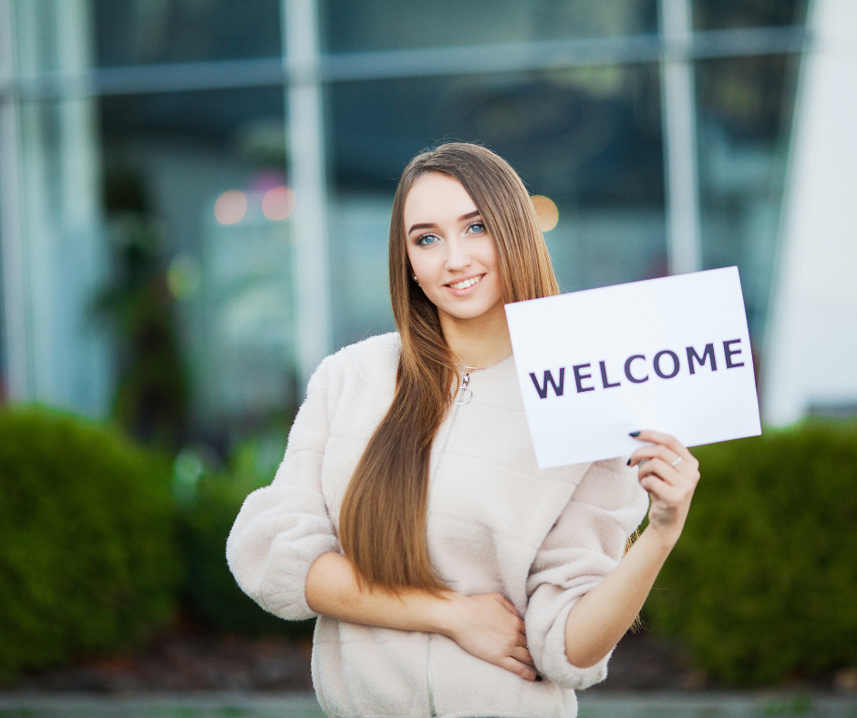 A person smiling and holding a welcome sign with a banner that reads "Welcome to the Company"