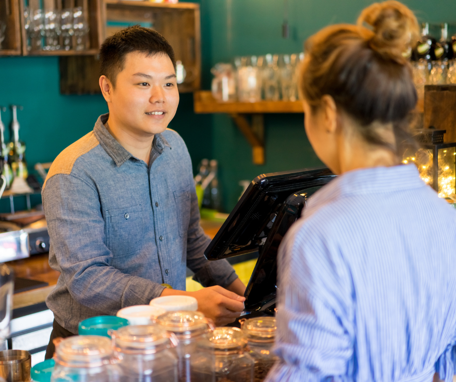A photo of a smiling First Watch employee taking customer orders at the counter