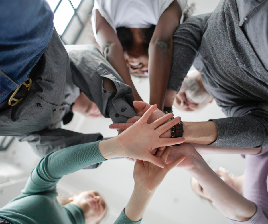 An image of a group of people, some of whom are holding hands in a circle, representing the concept of employee or employees depending on the context of the sentence.