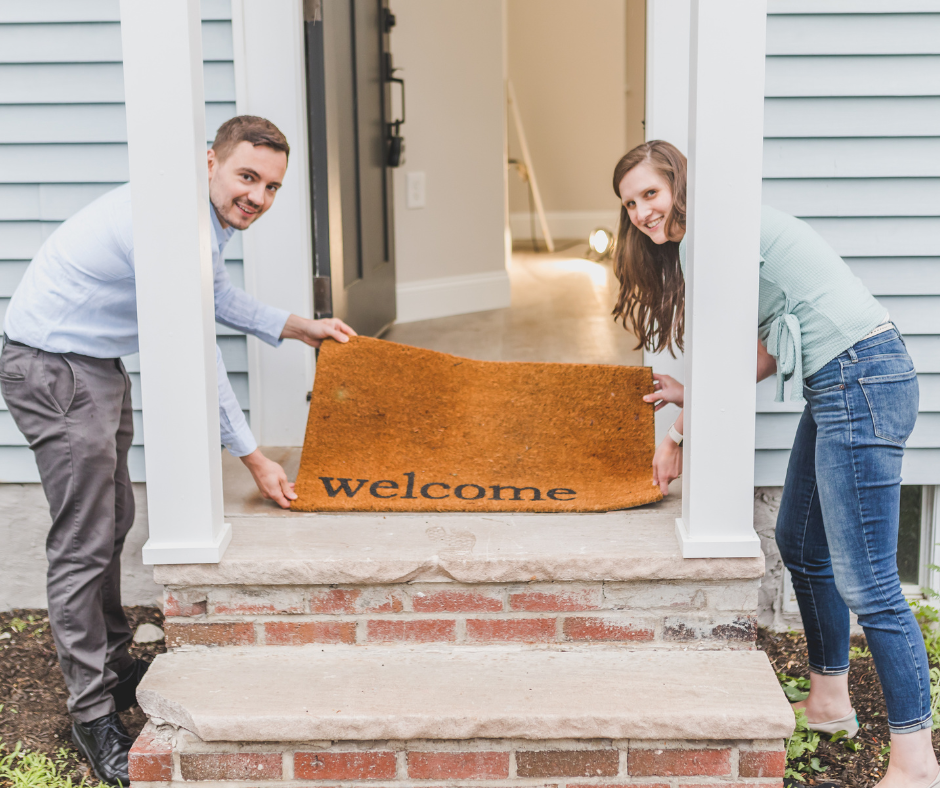An image of a team of employees gathered around a new colleague, smiling and holding a welcome sign to welcome a new employee